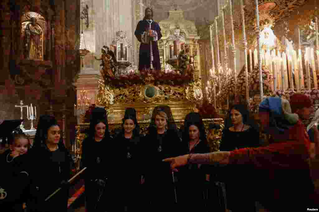 Penitentes con vestidos tradicionales de mantilla y 'Costaleros' pertenecientes a la hermandad de Los Gitanos esperan dentro de una iglesia para participar en una procesión del Domingo de Ramos, en Ronda, España.