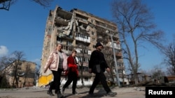 Local residents walk past an apartment building damaged during Russia's aggression against Ukraine, in Mariupol, Ukraine, April 15, 2022.