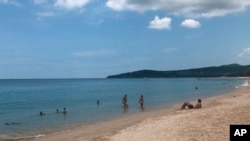 In this March 26, 2020, photo, tourists swim on a beach, Phuket, Thailand.