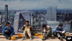 Construction workers eat lunch near a board with an artist's impression of the Central Business District outside a construction site in Beijing, China, April 6, 2017. 