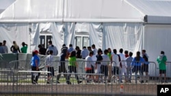 Niños inmigrantes centroamericanos hacen fila para entrar a una casa de campaña en el centro de detención temporal de Homested, Florida.