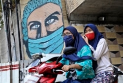 Dua perempuan mengenakan masker sambil naik motor di Jakarta, Indonesia (dok: AP/Dita Alangkara)