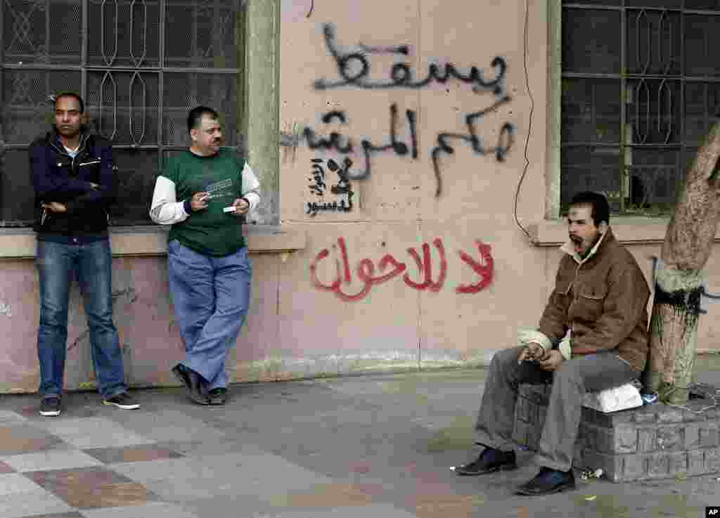Egyptian men stand near writing on a wall in Arabic that reads down with the leader's rule, no to the Muslim Brotherhood in Tahrir Square in Cairo, December 9, 2012.