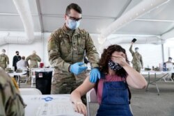 FILE - Leanne Montenegro covers her eyes while she receives the Pfizer COVID-19 vaccine at a FEMA vaccination center at Miami Dade College, in Miami, Florida, April 5, 2021.
