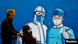 一名男子推着一位坐轮椅的妇女走过北京街头的一堵抗疫宣传墙。（2022年10月27日）