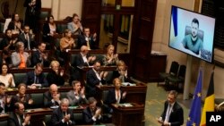 Belgium's Prime Minister Alexander De Croo, right, walks off the podium as Ukraine's President Volodymyr Zelenskyy watches from on screen, right, during a plenary session at the Belgian Federal Parliament in Brussels, Belgium, March 31, 2022.