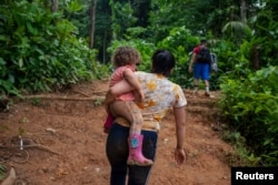 La migrante venezolana, Macyuli, sostiene a su hija mientras cruza el tapón del Darién junto a otros compatriotas.