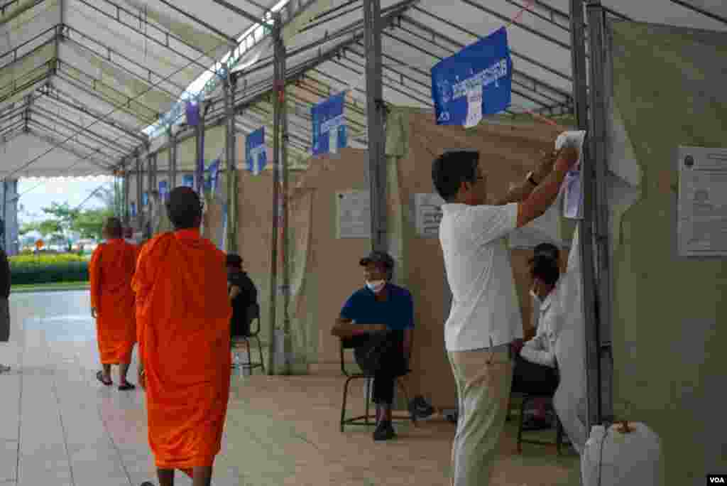 ព្រះសង្ឃនិមន្តកាត់បន្ទប់បោះឆ្នោត ខណៈបុរសម្នាក់ផ្ទៀងផ្ទាត់ឈ្មោះនៅក្នុងបញ្ជីឈ្មោះអ្នកបោះឆ្នោតនៅមណ្ឌលបោះឆ្នោតមួយកន្លែង មួយថ្ងៃមុនថ្ងៃបោះឆ្នោតឃុំសង្កាត់អាណត្តិទី ៥ នៅសង្កាត់ផ្សារកណ្តាលទី ១ ខណ្ឌដូនពេញ រាជធានីភ្នំពេញ ថ្ងៃសៅរ៍ ទី ៤ ខែមិថុនា ឆ្នាំ ២០២២។ (ខាន់ សុគុំមនោ/វីអូអេ)