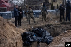 People stand next to a mass grave in Bucha, on the outskirts of Kyiv, Ukraine, Monday, April 4, 2022. (AP Photo/Rodrigo Abd)