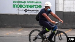 ARCHIVO - Un trabajador pedalea en su bicileta cerca de una valla con el logo de la firma Monómeros, en Barranquilla, Colombia, el 9 de octubre de 2021.