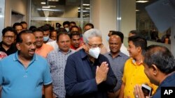In this handout picture provided by Sri Lanka's Ministry of Urban Development and Housing, the country's former President Gotabaya Rajapaksa, wearing a mask, is greeted upon his arrival at Bandaranaike International airport in Colombo, Sri Lanka, Sept. 3,
