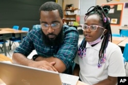 Ryan Johnson, a fifth-grade teacher at Pecan Park Elementary School, left, checks to see what homework his daughter, Rylei, is bringing home, as they prepare to leave Johnson's classroom in Jackson, Miss., Tuesday, Sept. 6, 2022. (AP Photo/Rogelio V. Solis)