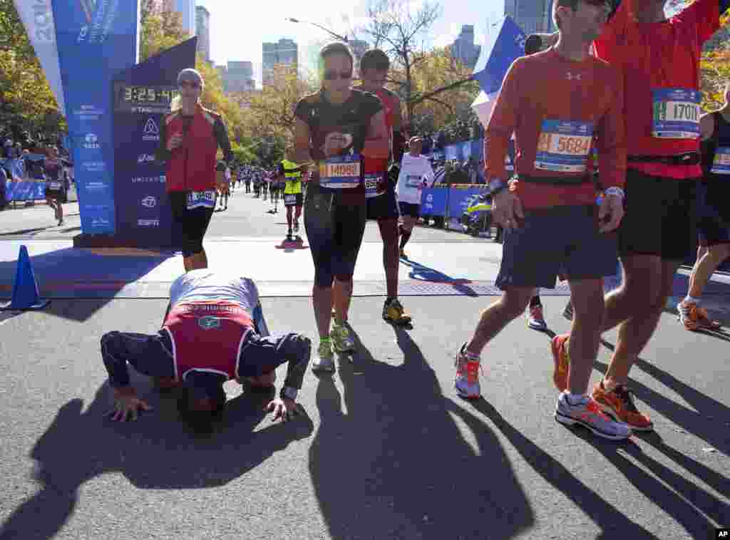 Un coureur embrasse le sol au moment où il franchit la ligne d'arrivée avec à ses cotes d&rsquo;autres participants du marathon de New York à New York, le 2 novembre 2014. 