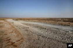 In this Tuesday, July 10, 2018 photo, where the Zayandeh Roud river once watered the region, desicated salt-laced fields surround the Gavkhouni wetlands, outside town of Varzaneh, Iran.