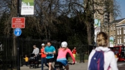 Las personas observan el distanciamiento social cuando pasan por las puertas cerradas del Parque Brockwell en Londres, cerrado durante la noche por el consejo local para ayudar a detener la propagación del coronavirus.