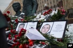 Photos of Lt.Col. Oleg Peshkov, left, and sailor Alexander Pozynich are placed at a monument to Soviet Officers with flowers and a toy jet made of paper outside Russian Army General Staff headquarters in Moscow, Nov. 26, 2015.
