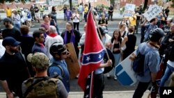 FILE - A white supremacists carries the Confederate flag as he walks past counter demonstrators in Charlottesville, Va., Aug. 12, 2017.