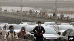People wearing face masks walk past cars clogged with heavy traffic on a road as Beijing is hit by polluted air and sandstorm, May 4, 2017. Authorities in Beijing issued a blue alert on air pollution as sandstorm swept through the Chinese capital city on 