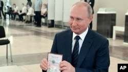 Russian President Vladimir Putin shows his passport to a member of an election commission as he arrives to take part in voting at a polling station in Moscow, Russia, July 1, 2020.