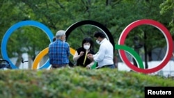 People chat next to Olympic Rings monument outside the Japan Olympic Committee (JOC) headquarters near the National Stadium, the main stadium for the 2020 Tokyo Olympic Games that have been postponed to 2021, in Tokyo, June 23, 2021. June…