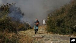 A migrant holds her baby as she runs to avoid a small fire in a field near Mytilene town, on the northeastern island of Lesbos, Greece, Saturday, Sept. 12, 2020. 
