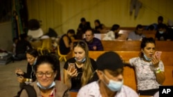 Inmigrantes esperan y hablan con sus familiares por teléfono en un almacén administrado por el grupo sin fines de lucro Mission: Border Hope, en Eagle Pass, Texas, el 23 de mayo de 2022. (Foto AP/Dario López-Mills)