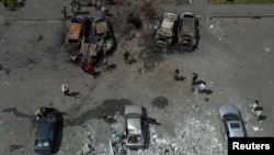 People stand next to cars destroyed by a Russian missile strike at a residential area in Kharkiv, Ukraine, June 26, 2022. 