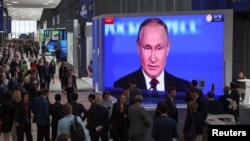 Participants at the St. Petersburg International Economic Forum gather near a screen showing Russian President Vladimir Putin