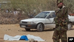 A member of the Kenyan security forces speaks on a telephone next to the body of one of those killed, outside the African Inland Church in Garissa, Kenya, July 1, 2012. 