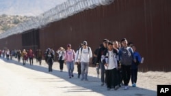 一群來自中國尋求庇護的移民穿越美國與墨西哥邊境後在加州賈昆巴附近沿著隔離牆行走。 (2023年10月24日)