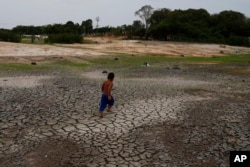 A little boy walks across a dry, cracked area of the Negro River near his houseboat during a drought in Manaus, Amazonas state, Brazil, Monday, Oct. 16, 2023. (AP Photo/Edmar Barros)