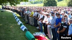 People pray near coffins at a graveyard during a mass funeral in Potocari near Srebrenica, Bosnia and Herzegovina July 11, 2020.