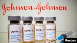 Vials and medical syringe are seen in front of J&J logo in this illustration