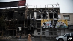In a photo taken Nov. 18, 2019, and released by the Iranian Students' News Agency, ISNA, people walk past buildings which burned during protests that followed the authorities' decision to raise gasoline prices, in the city of Karaj, west of Tehran.
