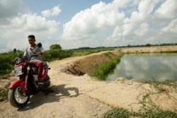 Chhum Phirom, 26, sits on a motorcycle near his fish pond in Peamror district, Prey Veng province, Cambodia, on July 22, 2020. (Aun Chhengpor/VOA Khmer)