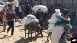 ሰዎች ከእስታየሽ ተብሎ በሚታወቀው የምግብ ማእከል በደንከና ቀበሌ መከት ወረዳ የምግብ እርዳታ ተቀብለው ወደየመኖርያቸው በሚጉጓዙበት ጊዜ የተነሳ ፎቶ[አሶሽየትድ ፕረስ/AP]
