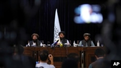FILE - In front of a Taliban flag, Taliban spokesman Zabihullah Mujahid, center, speaks at his first news conference, in Kabul, Afghanistan, Aug. 17, 2021. 