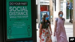 FILE - Two women walk past a social distance sign at City Creek Center in Salt Lake City, Utah, May 6, 2020.