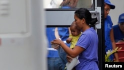 Archivo. Una mujer y su hijo suben a un bus que lleva migrantes deportados a una estación en el aeropuerto internacional de San Pedro Sula. Honduras. Julio, 2014.