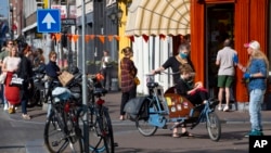 People, some wearing face masks, observe social distancing to prevent the spread of the coronavirus when standing in line to buy traditional King's Day pastry in Amsterdam Netherlands, Monday, April 27, 2020. The Dutch national birthday party was a…