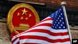 FILE - An American flag is flown next to the Chinese national emblem during a welcome ceremony for visiting U.S. President Donald Trump outside the Great Hall of the People in Beijing, Nov. 9, 2017.