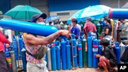 A man carries an oxygen tank as he walks past people waiting with oxygen tanks in need of refill outside the Naing oxygen factory at the South Dagon industrial zone in Yangon, Myanmar, Wednesday, July 28, 2021. Myanmar is currently reeling from…
