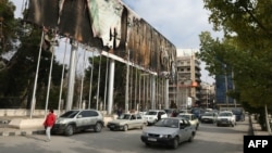 People drive past a burnt billboard bearing a portrait of Syrian President Bashar al-Assad at Aleppo's Saadallah al Jabiri Square on Dec. 5, 2024.