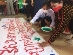 ស្រ្តីម្នាក់ កំពុង​ផ្តិត​បាតដៃ​នឹង​ថ្នាំពណ៌​លើ​ផ្ទាំង​ក្រណាត់​ដែល​មាន​សរសេរ​ពាក្យស្លោក ក្នុង​ទិវា​អន្តរជាតិ​«បញ្ឈប់​ការប្រើប្រាស់​អំពើ​ហិង្សា​លើ​អ្នករកស៊ី​ផ្លូវភេទ» នៅ​ខណ្ឌឫស្សីកែវ រាជធានី​ភ្នំពេញ នៅ​ថ្ងៃទី១៦ ខែធ្នូ ២០២១។ (មាស មល្លិកា/វីអូអេ)