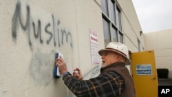 FILE - Tom Garing cleans up racist graffiti painted on the side of a mosque in what officials are calling an apparent hate crime, Feb. 1, 2017, in Roseville, Calif. The Tarbiya Institute was spray-painted with a dozen obscene and racist slurs. 