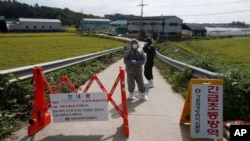 Quarantine officials wear protective gear as a precaution against African swine fever at a pig farm in Paju, South Korea, Sept. 17, 2019. The notice reads: "Under quarantine."