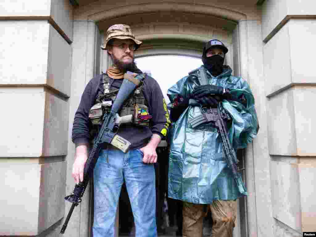 Protesters with long guns shelter from the heavy rain during a protest against Governor Gretchen Whitmer's extended stay-at-home orders to slow the spread of the coronavirus disease (COVID-19), at the Capitol building in Lansing, Michigan.