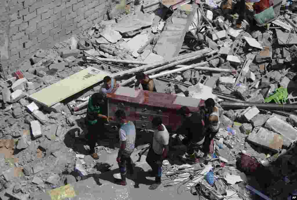 Issal oilasi vakillari vayron bo'lgan uy xarobalari orasidan yaroqli ro'zg'or jihozlarini olib chiqmoqda, G'azo, 2-avgust, 2014-yil.