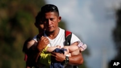 El migrante hondureño Selvin Hernández lleva a Mayra Irene, hija de otro migrante, en medio de una caravana que intenta llegar a Estados Unidos, cerca de El Cinchado, Guatemala.