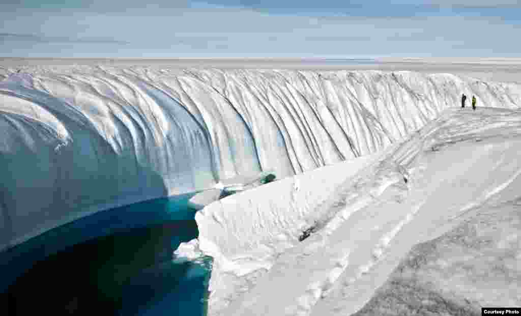 Over the course of several years, turbulent water overflow from a large melt lake carved this 60-foot deep canyon. Note the people for scale. (Photo courtesy of Ian Joughin)